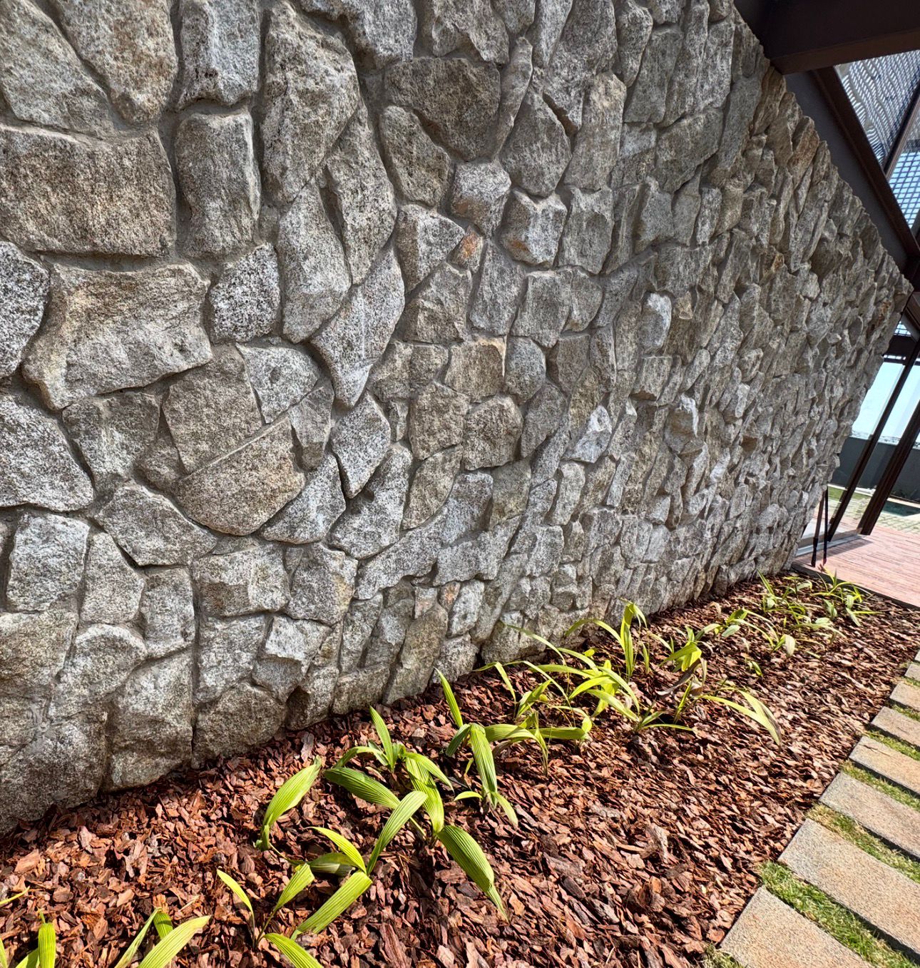 Jardim linear implantado junto a parede de pedra natural